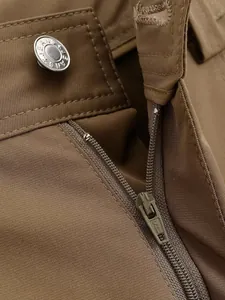 Macro detailed view of the metal zipper and silver button on khaki cargo trousers