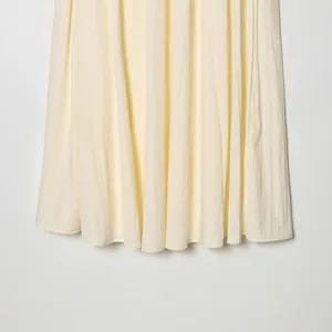 Detail of a light yellow flowing midi skirt with soft pleated fabric texture.