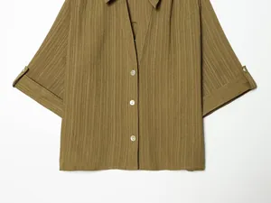 Detail view of olive green pleated shirt with button-down collar and rolled sleeves.