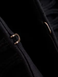 Macro detail of a bronze metal hook-and-eye closure on a black textured slim-fit blazer.