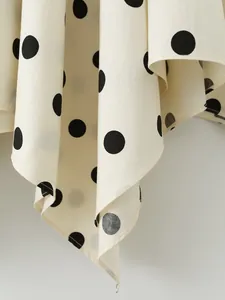 Close-up detail showing the cream fabric with black polka dots and asymmetrical skirt hemline