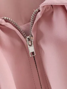 Gros plan d'une fermeture éclair en métal argenté sur un blouson aviateur rose.