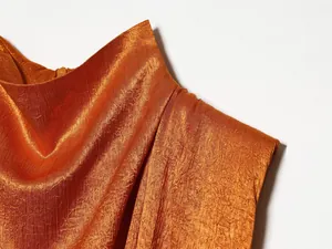 Gedetailleerde close-up van de gekreukelde zijde-satijn textuur van een oranje top