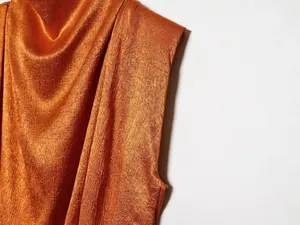 Detailopname van oranje satijnen blouse met elegante gekreukte textuur en glanzende finish