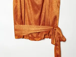 Detailopname van een oranje satijnen top met getextureerde stof en een strikdetail