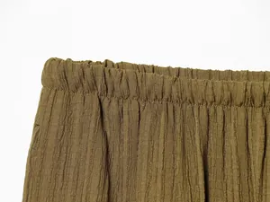 Detailed macro view of elastic waistband on olive green pleated wide-leg trousers.