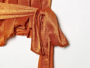 Detailopname van een oranje satijnen top met een gestrikte strik aan de zijkant.