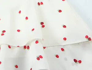 Close-up detail showing the strawberry print and layered satin texture of the white garment.
