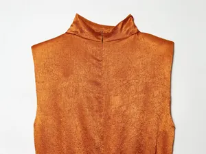 Detailopname van een mouwloze top met hoge nek in glanzende koperen satijnstructuur