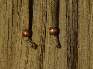 Close-up detail of olive green crinkle fabric with braided drawstring and wooden beads.