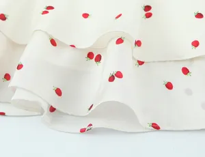 Detailed close-up of red strawberry print on white tiered satin fabric with soft texture
