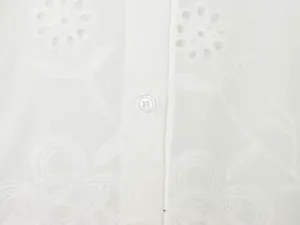 Detailopname van fijn wit bloemenborduurwerk en knoop op een vrouwelijke witte blouse
