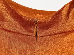 Close-up detail van een verborgen rits op een oranje satijnen getextureerde blouse.