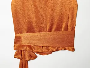 Detailopname van oranje satijnen stof met een elegant strikdetail op een top