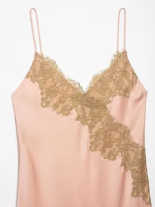 Detailed macro view of a pink satin slip dress with golden lace trim and thin straps