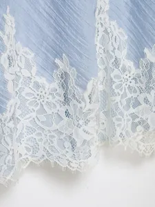 Macro detail of elegant white floral lace embroidery on light blue textured fabric skirt hem