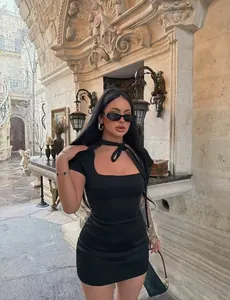Elegante vestido ajustado negro con lazo en el cuello en entorno arquitectónico