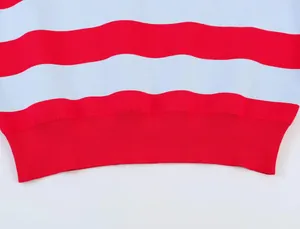 Gros plan sur l'ourlet côtelé d'un pull en tricot rayé rouge et blanc.