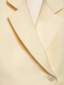 Close-up macro view of minimalist beige blazer lapel and elegant pearlescent button detail