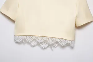 Detail view of the intricate white lace trim on the hem of a cream cropped blazer jacket.
