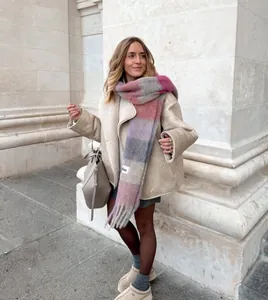 Detailed view of a woman wearing a beige faux shearling coat with a plaid scarf outdoors