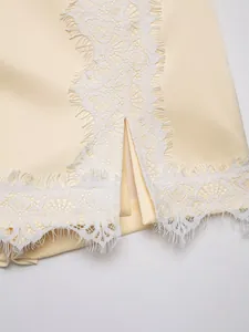 Close-up of white eyelash lace trim on a cream satin skort hem with a stylish slit detail.