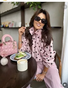 Detalle de chaqueta rosa con lunares, cuello alto y lazo en una cafetería elegante