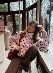Vista detallada de una chaqueta rosa con lunares usada por una mujer en un café acogedor