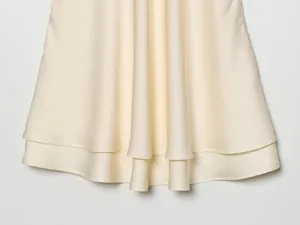 Detailopname van de dubbellaagse zoom van een luxe crème satijnen slipdress.