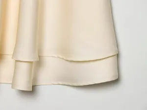 Macro-opname van de elegante dubbellaagse zoom van een crèmekleurige zijden satij zijden satijnen jurk