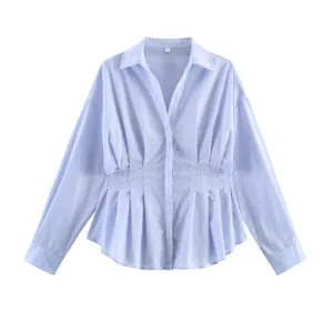 Dettaglio della polo a maniche lunghe azzurra con elegante design a vita a pieghe.