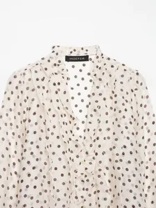 Detailweergave van een witte blouse met bruine stippen en elegante gelaagde ruches
