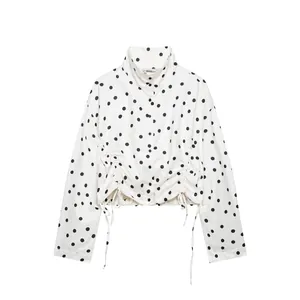 Detalle de una chaqueta blanca de lunares con cuello alto, botones y dobladillo fruncido