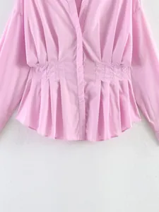 Dettaglio ravvicinato di una camicia rosa con vita a pieghe e tessuto setoso.