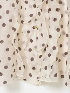 Detailopname van ruches en stippenpatroon op een ivoorkleurige blouse van dichtbij