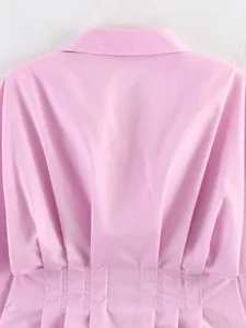 Dettaglio di una polo rosa a maniche lunghe con design della vita arricciata.