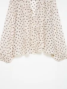 Detailopname van een crème blouse met stippen met gelaagde ruches en lantaarnmouwen