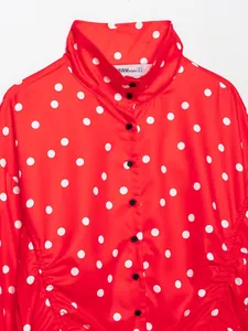 Detalle de una blusa roja de cuello alto con lunares blancos y volantes fruncidos.
