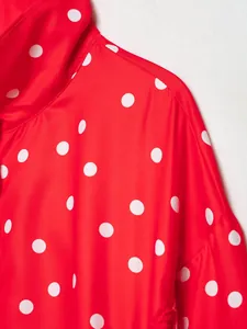 Detalle de cerca de una chaqueta roja de cuello alto con estampados de lunares blancos.