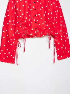 Vista detallada de una blusa roja con lunares, dobladillo fruncido y cordón ajustable