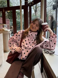 Chaqueta rosa con lunares, cuello con lazo y botones en un entorno de cafetería
