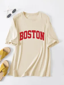 Detailopname van een beige oversized T-shirt met rode Boston-print en zomeraccessoires.