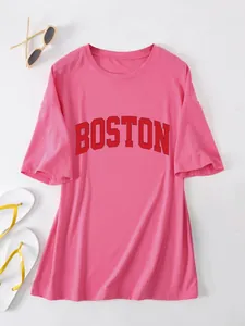 Detail van een roze oversized T-shirt met een gedurfde rode BOSTON grafische print op de borst.