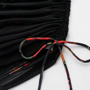 Detailansicht der schwarzen Netzraffung und des floral bedruckten Bandes eines Badeanzugs