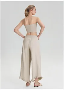 Achteraanzicht vrouw in beige top en wijde 7/8 sportbroek met ruffels voor yoga
