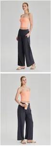 Vue complète d'une femme en haut de yoga corail sans bretelles et pantalon gris large.