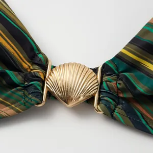 Detail shot of a golden shell-shaped buckle on a color-blocking striped swimsuit