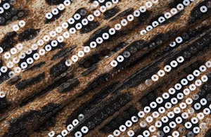 Macro detail showing sparkling silver sequins stitched on leopard print mesh fabric texture