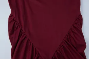 Dettaglio della vita a V plissettata su un abito lungo bordeaux aderente senza maniche.