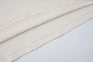 Primer plano de la costura overlock profesional en el dobladillo de tela color blanco roto